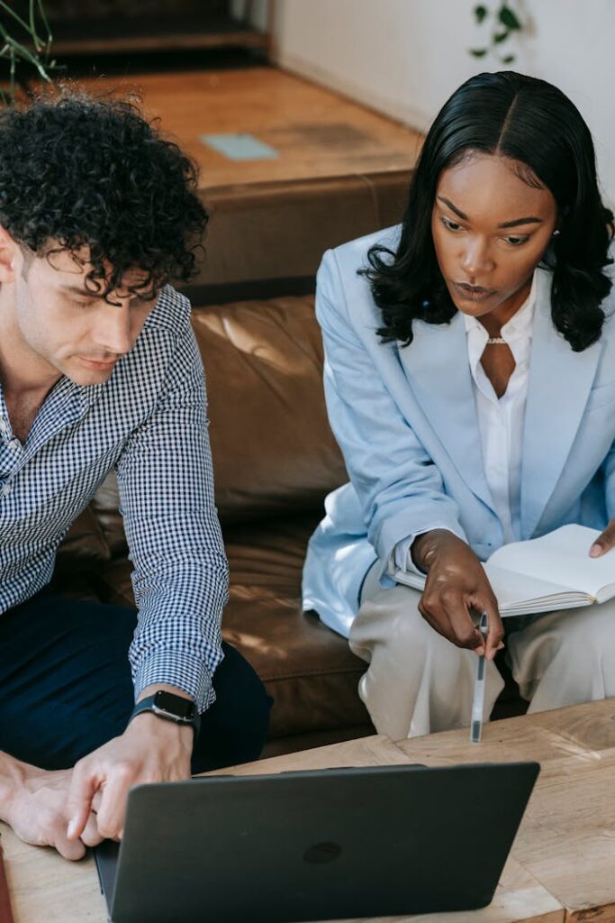 Two professionals working together closely on a laptop in a collaborative office setting.
